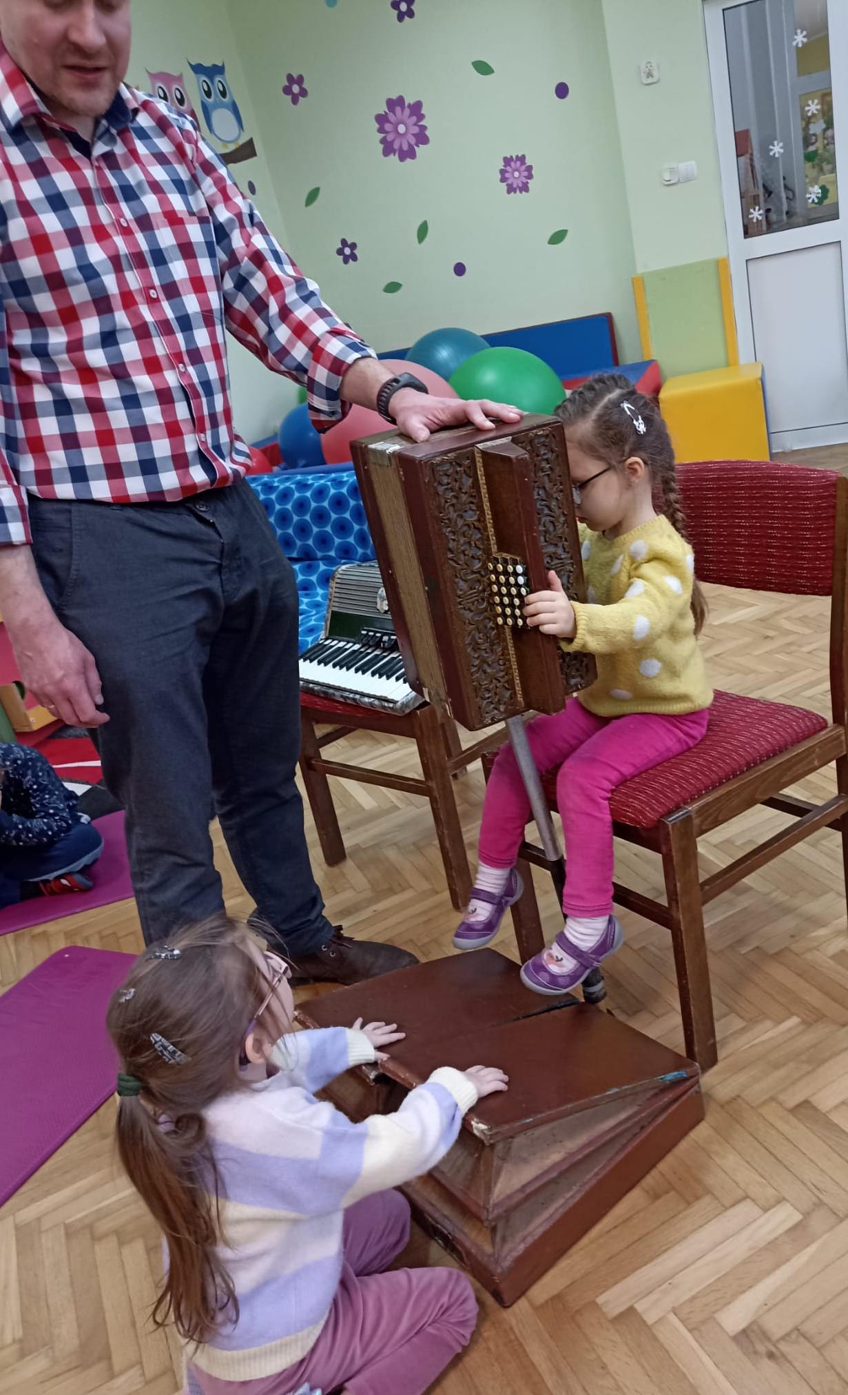 Weronika i Maja przy wsparciu pana Piotra, próbują wspólnymi siłami wydobyć dźwięk z harmonii