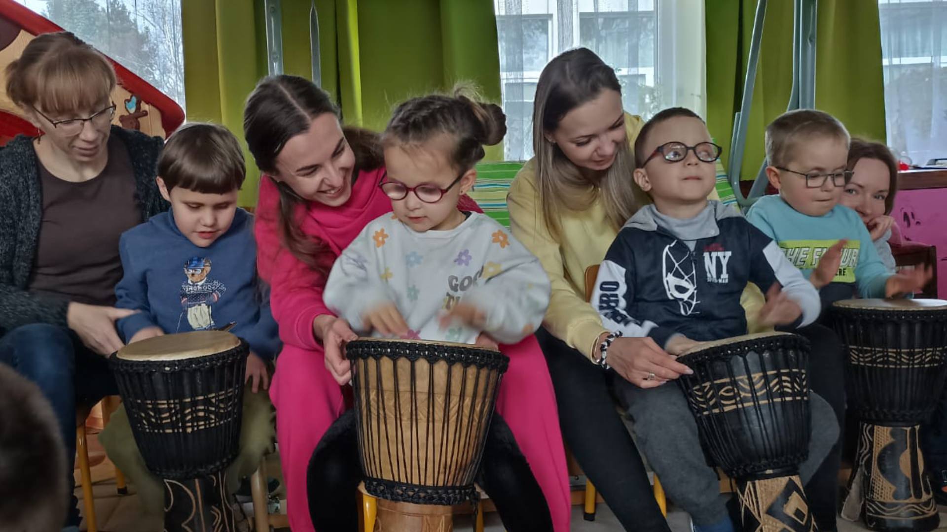 Grupka dzieci grająca na bębnach i wspierający ich dorośli
