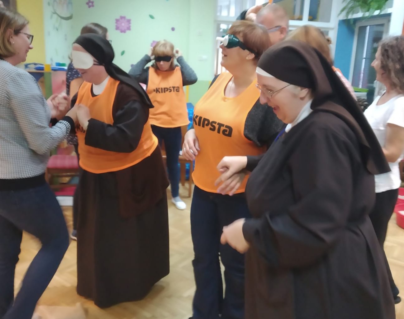 Grupa nauczycieli w opaskach i symulatorach prowadzona przez innych nauczycieli.
