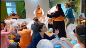 Nauczyciele w opaskach na oczach bawią się folią i balonami.