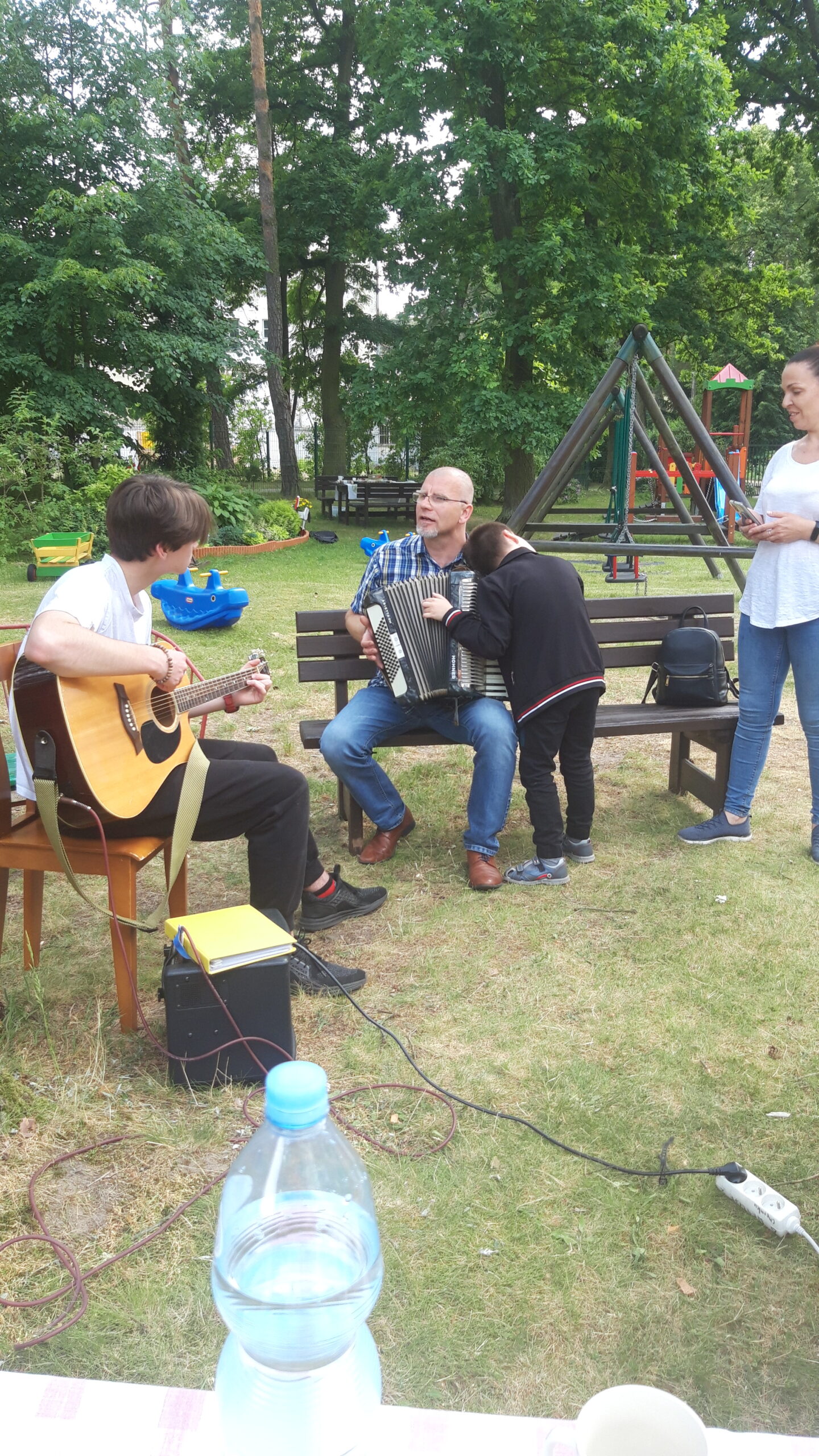 Chłopiec gra na gitarze, jeden z rodziców gra na akordeonie.
