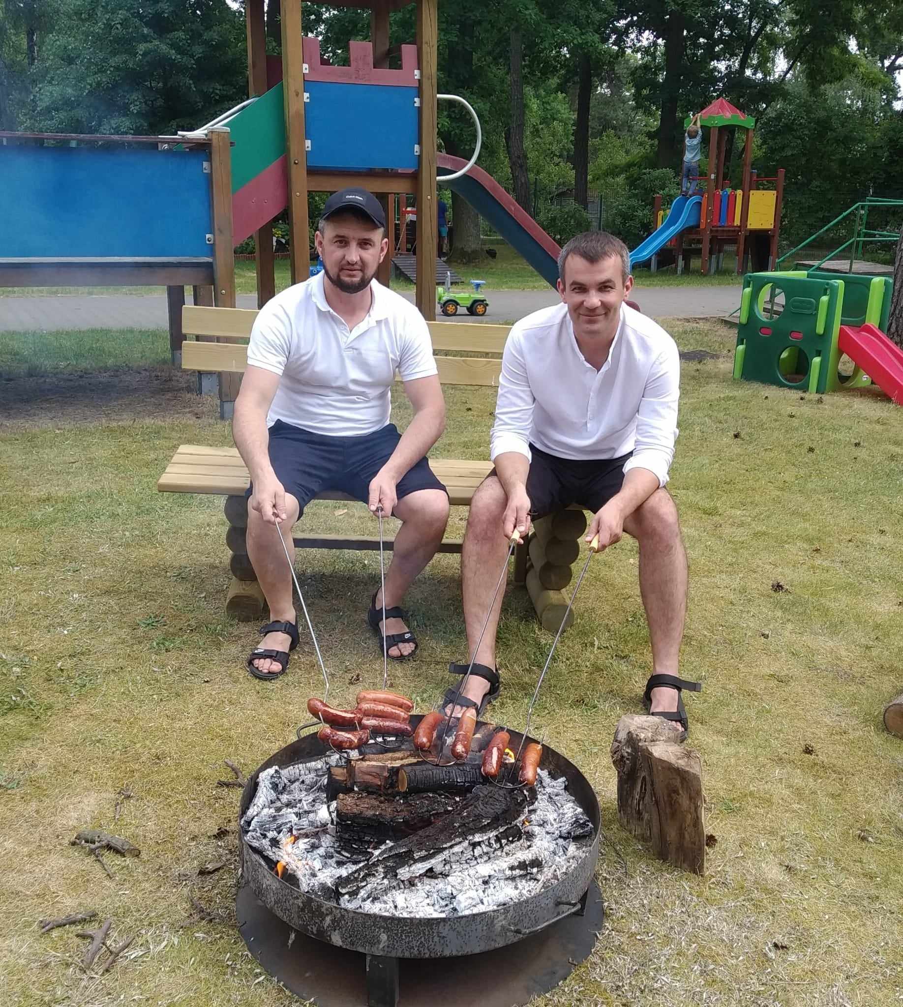Dwóch ojców piecze kiełbaski nad ogniskiem.