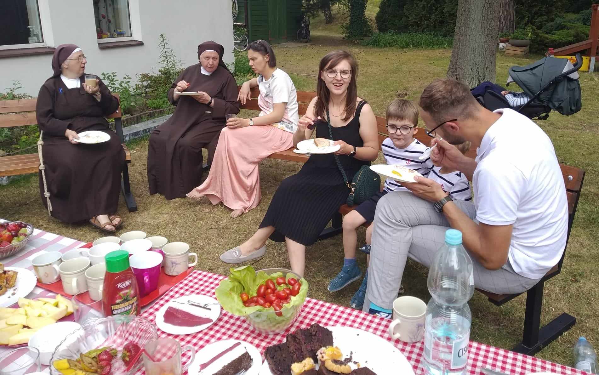 Siostry, rodzice, nauczyciele i dzieci jedzą posiłek.