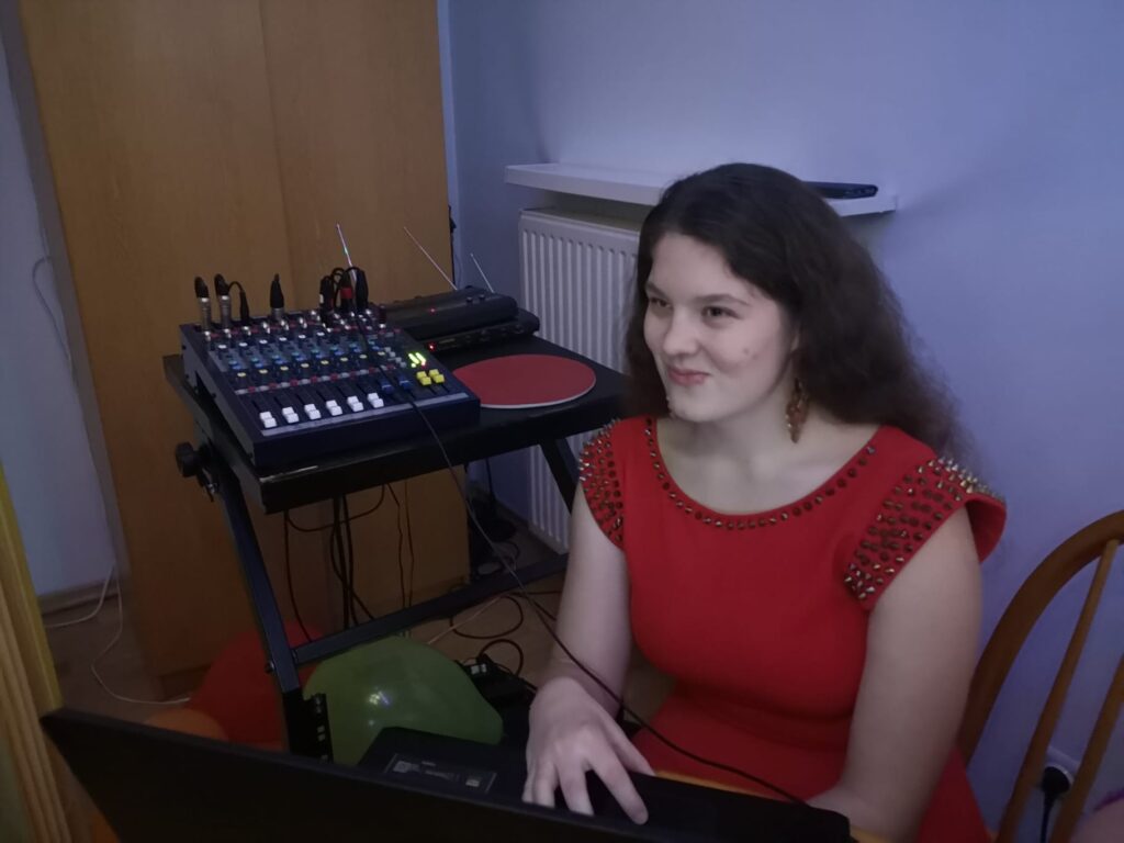 Wychowanka Ewa ubrana w czerwoną sukienkę  siedzi przy aparaturze i czuwa nad muzyką
