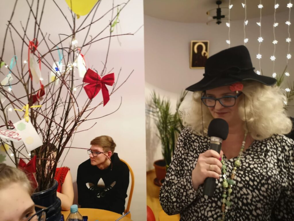 Pani Asia trzyma w ręku mikrofon i  zaprasza do konkursu 8 odważnych dziewcząt