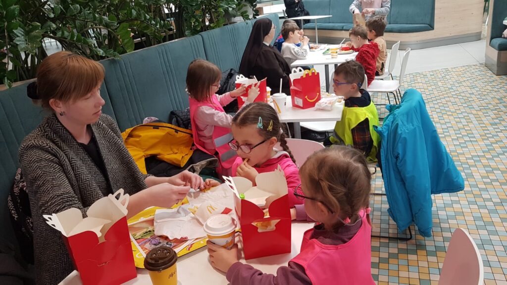 Przedszkolaki siedzą przy stołach, na których jest jedzenie z Mc. Donalds'a
