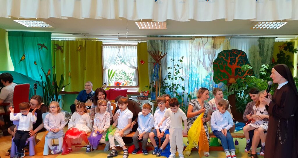 Przedszkolaki i panie z kolorowymi chusteczkami zawiązanymi na rękach podczas występu