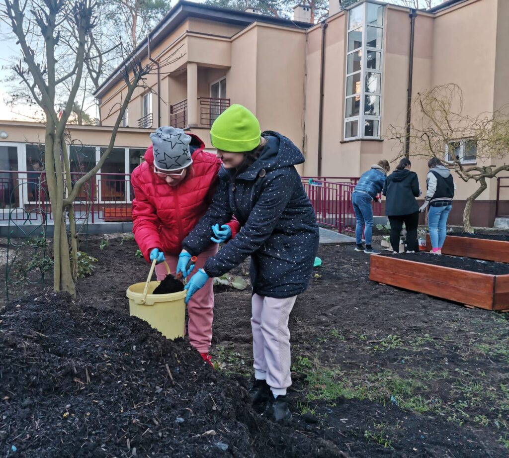 Dziewczęta przenoszą ziemię do drewnianej skrzyni