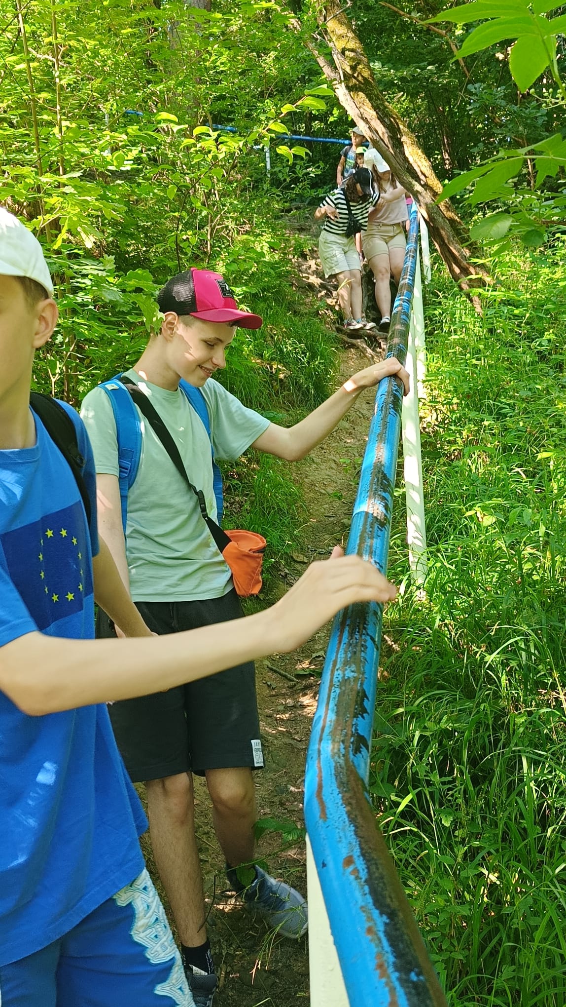 Uczniowie idą stromą ścieżką w lesie.