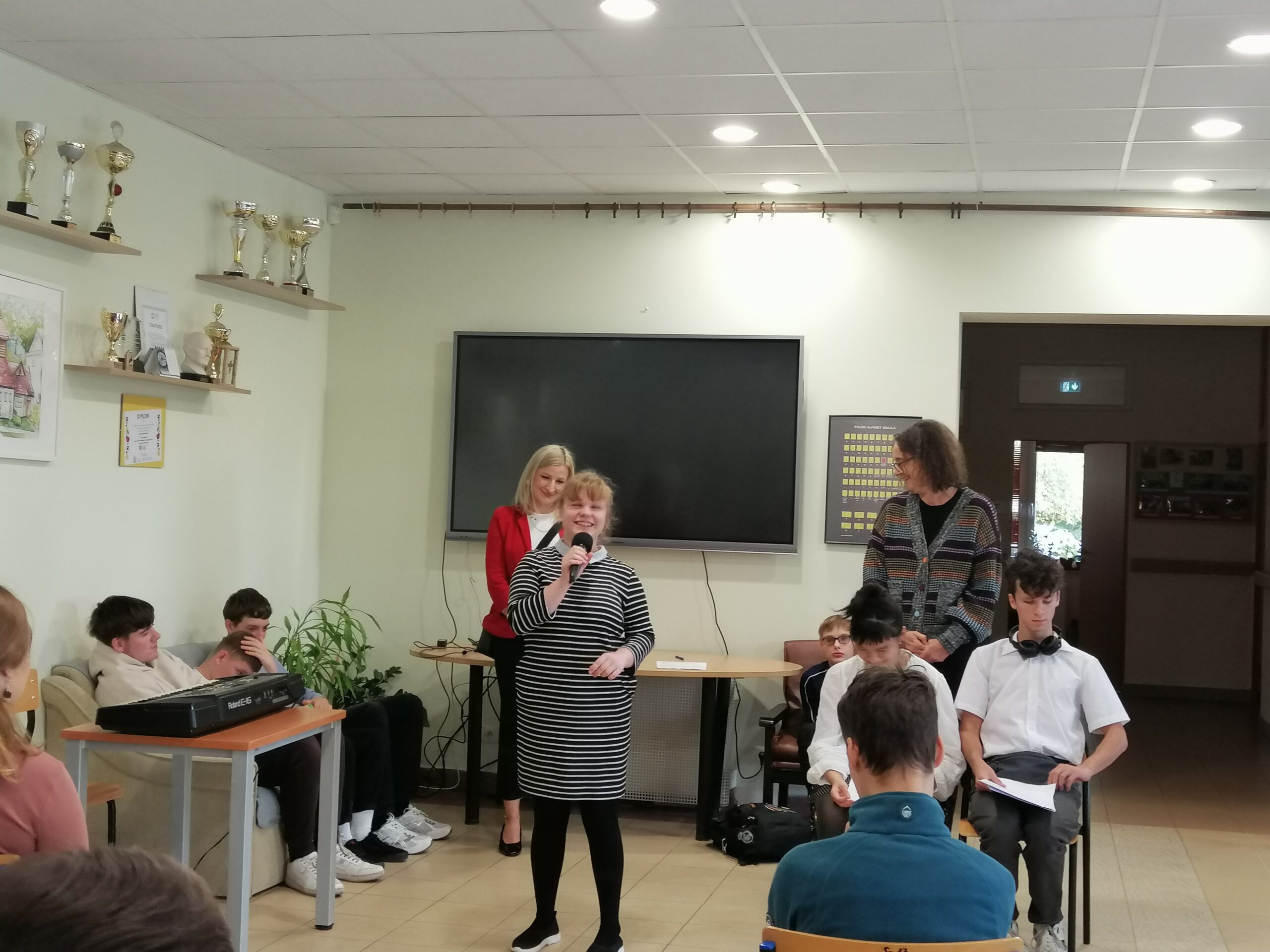 Uczennica klasy pierwszej liceum na korytarzu w szkole średniej opowiada o sobie. Wszyscy uważnie słuchają opowiadań i wierszy.