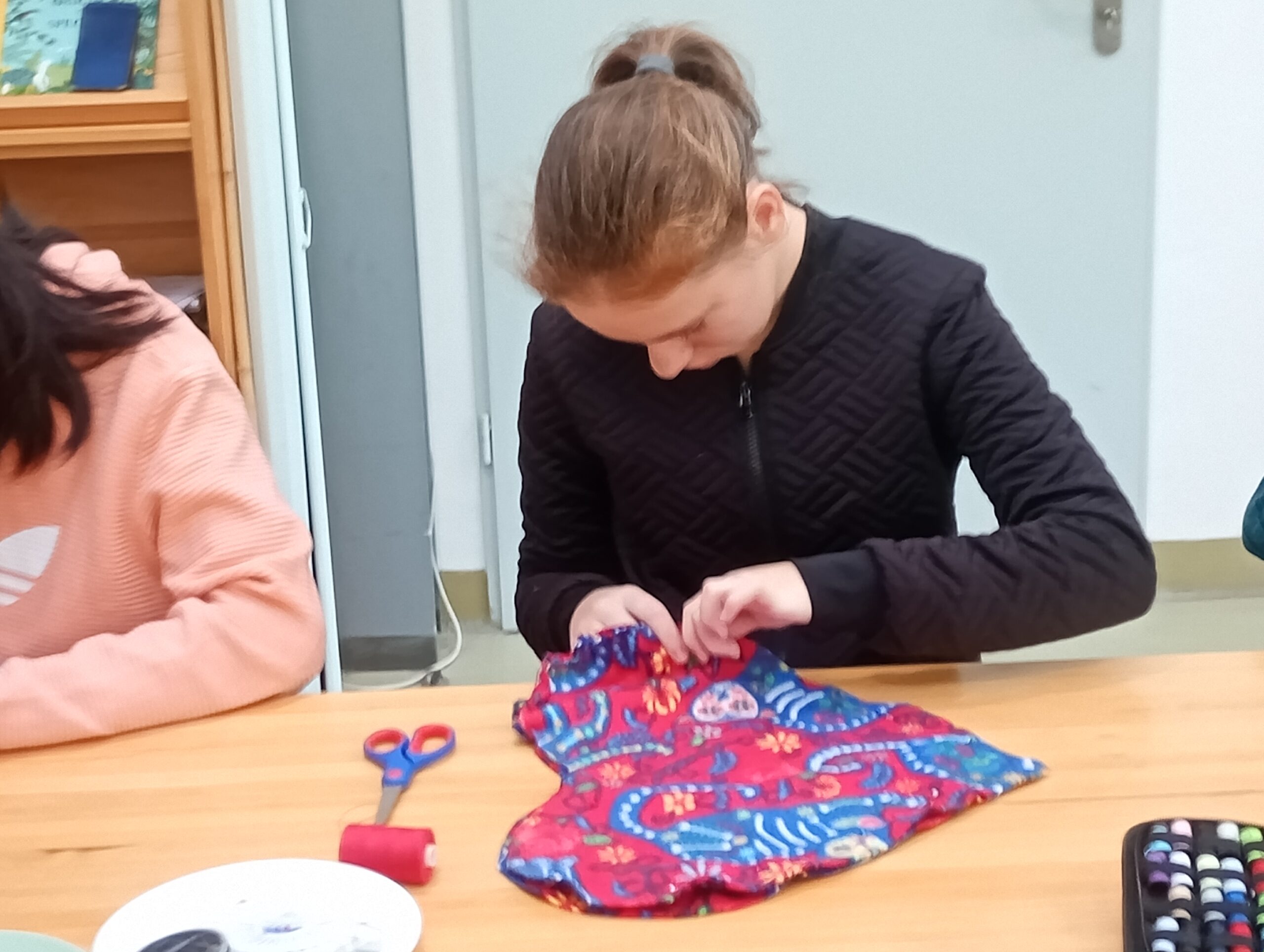 Uczennica zszywa wykrojoną w kształcie serca poduszkę.