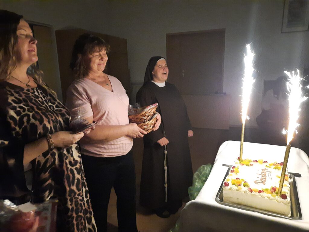 Siostra Marta z paniami Małgosią i Dorotą w trakcie śpiewania 100 lat przy torcie na którym palą się świece fontanny