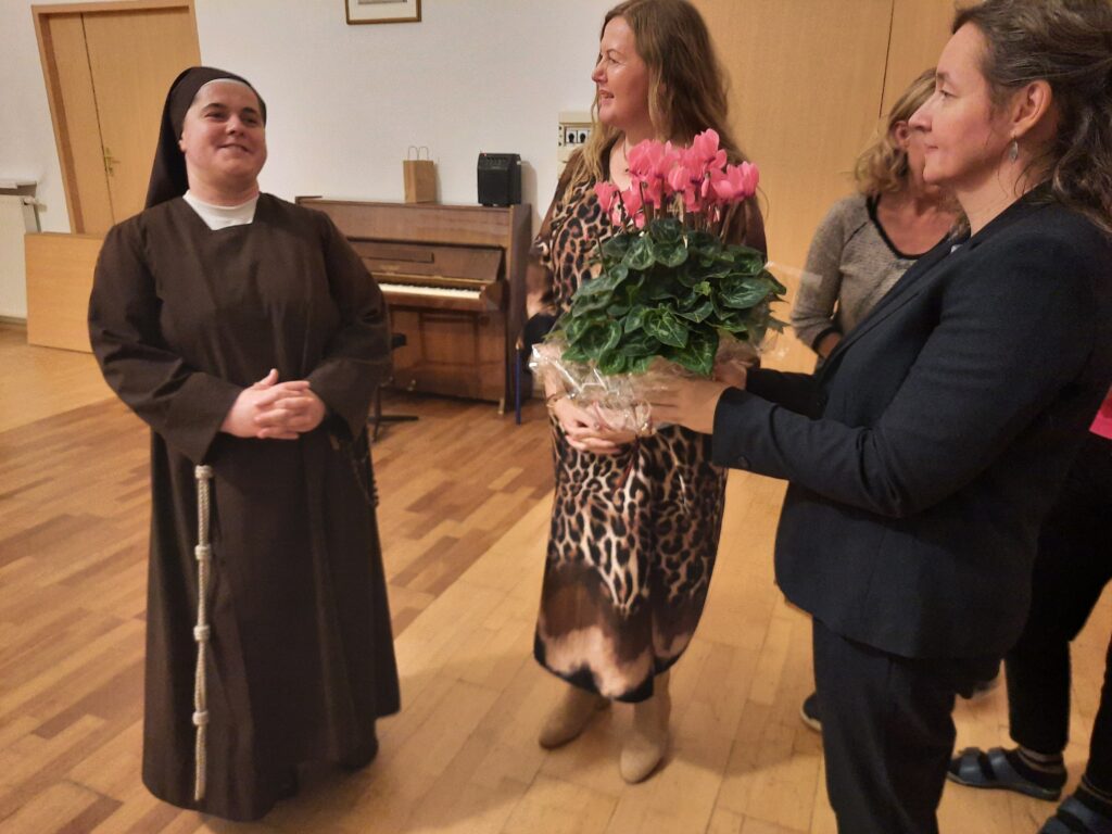 Pani Agata z panią Małgosią składają życzenia Siostrze Marcie i wręczają różowe fiołki