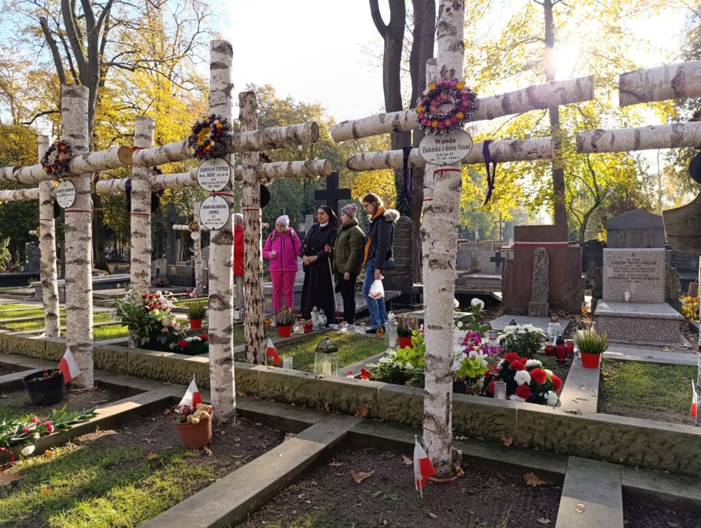 Dziewczęta stoją przy grobach na Powązkach