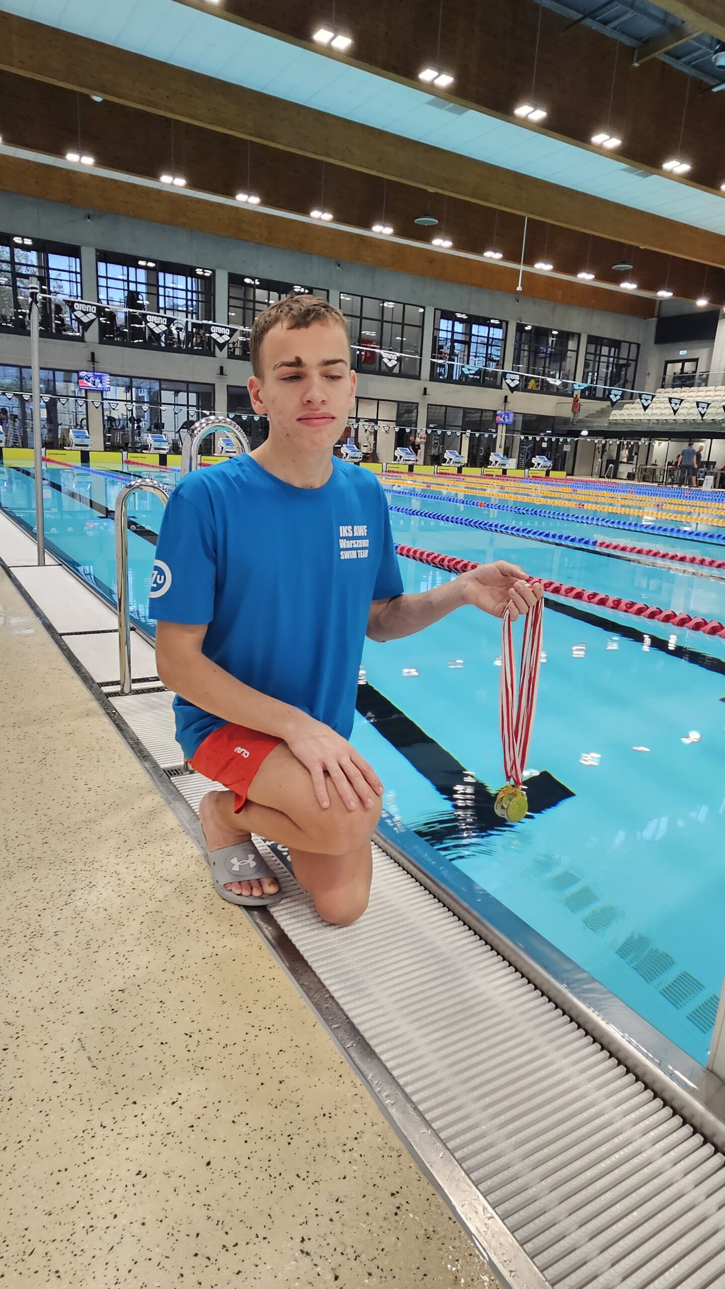 Alex z medalami przy basenie.