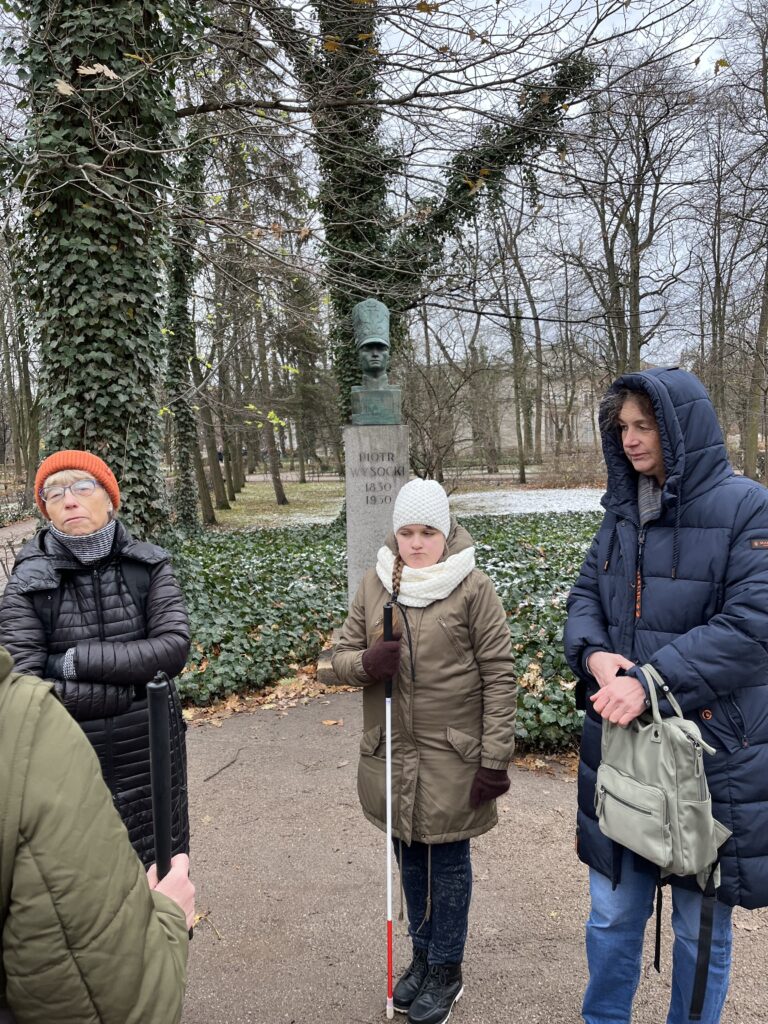 Uczennica wraz z nauczycielami przed pomnikiem Piotra Wysockiego.