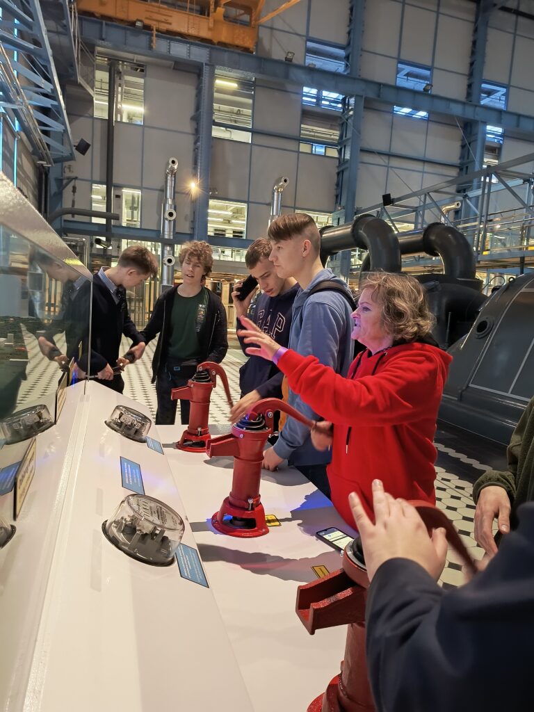 Uczniowie 2 i 5 klasy technikum wraz z Panią Hanna która opisuje urządzenia modelujące działanie urządzeń dostarczających wodę w muzeum nauki