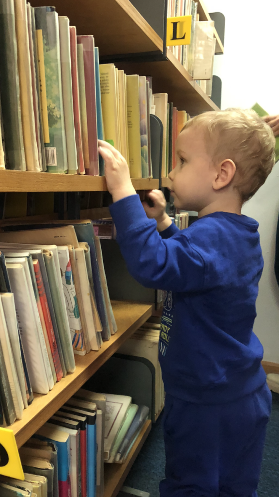 Chłopiec ogląda książki na regale bibliotecznym.
