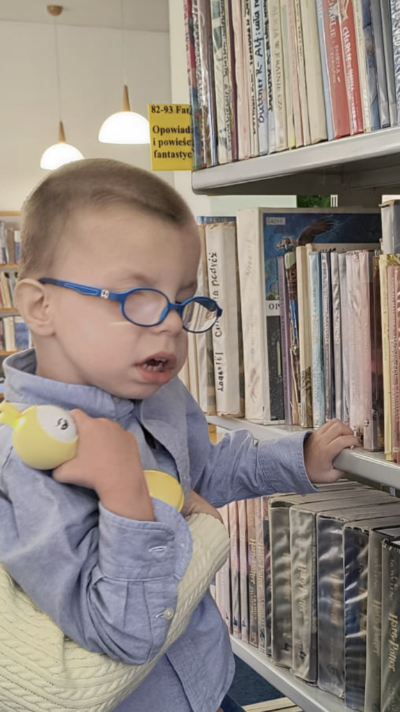 Chłopiec ogląda książki na regale bibliotecznym.