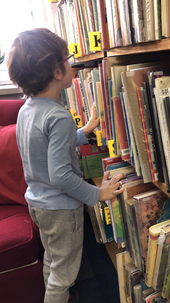 Chłopiec ogląda książki na regale bibliotecznym.