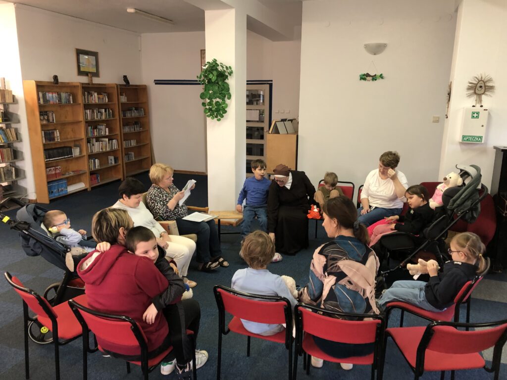 Dzieci i nauczyciele siedzący na krzesłach w bibliotece.