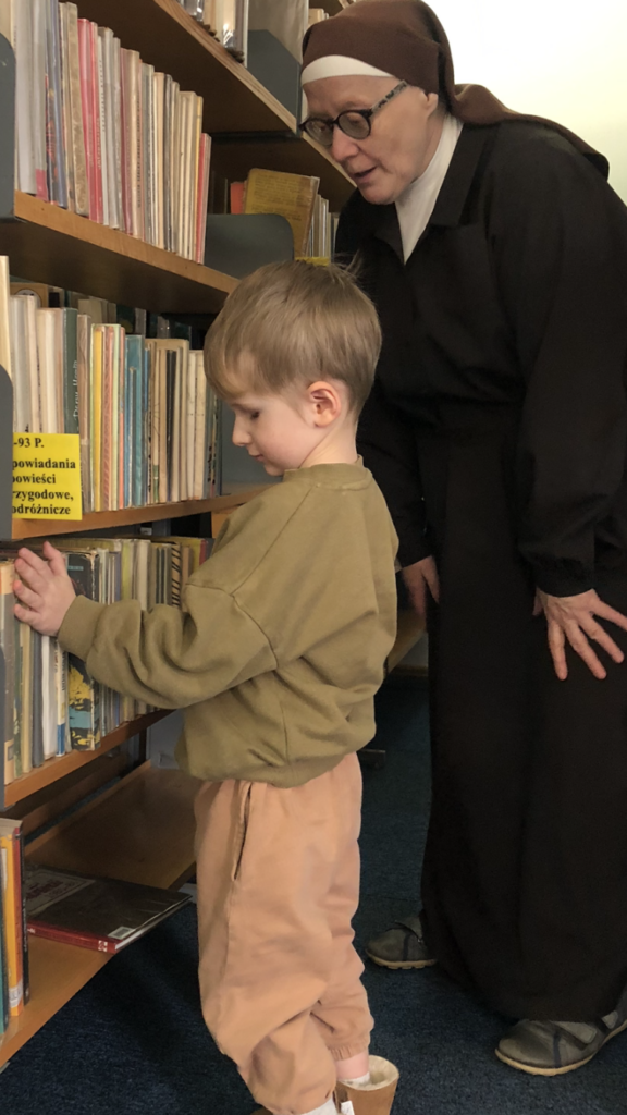 Chłopiec z Siostrą ogląda książki na regale bibliotecznym.