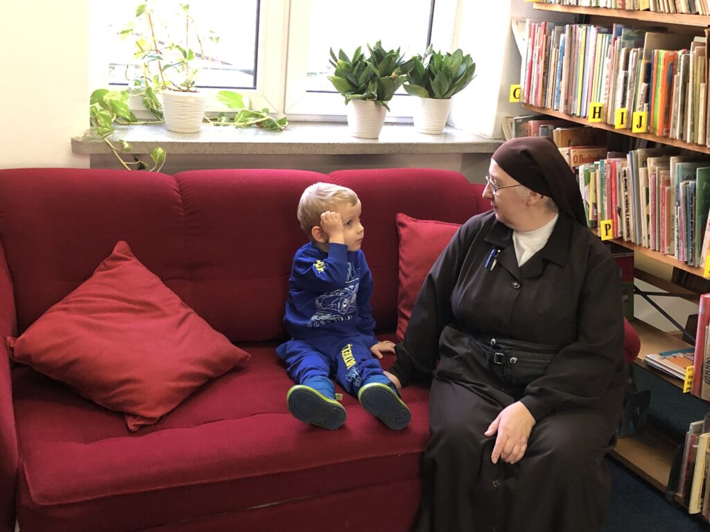 Chłopiec siedzi na kanapie z Siostrą. Z boku regał z książkami.