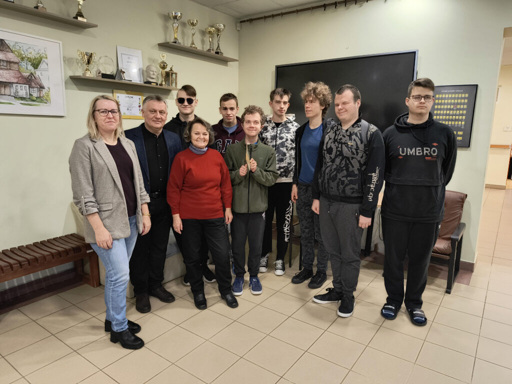 Uczniowie 2, 4 i 5 klasy wraz z dyrektorem i nauczycielami będącymi opiekunami na wyjeździe stoją uśmiechnięci w szkole ponadpodstawowej.