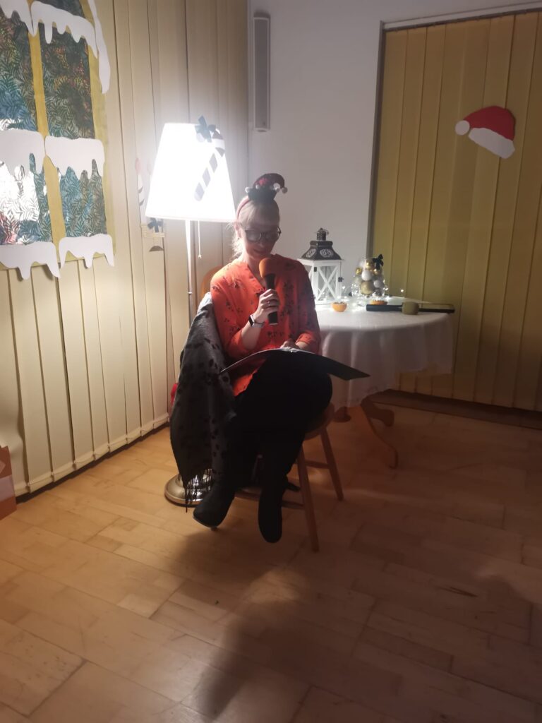 Pani Basia siedzi na krześle i  czyta historię Biskupa z Miry