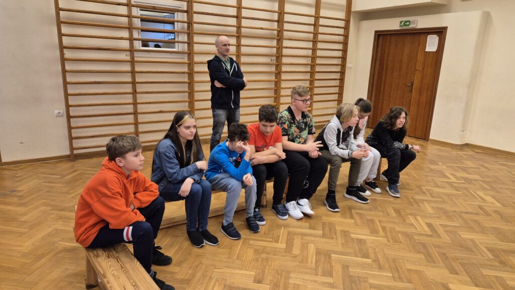 Uczniowie 7 klasy i 6 klasy na sali sportowej słuchają opowiadania Siostry.