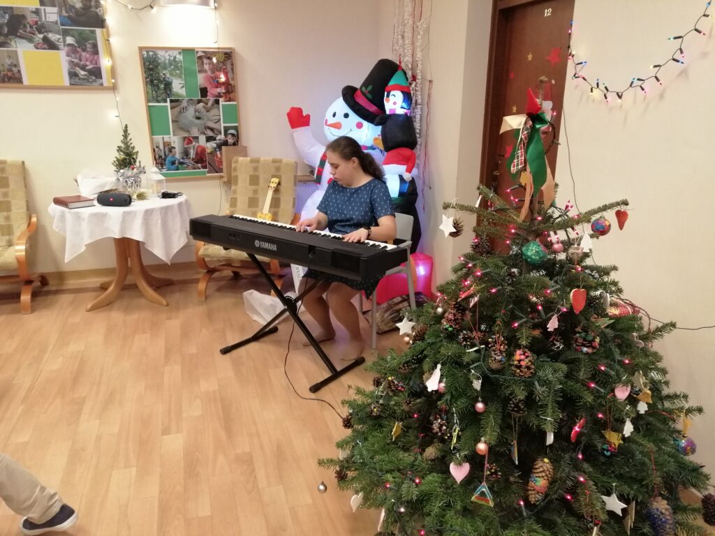 Amina gra kolędy na organach. Obok stoi choinka.