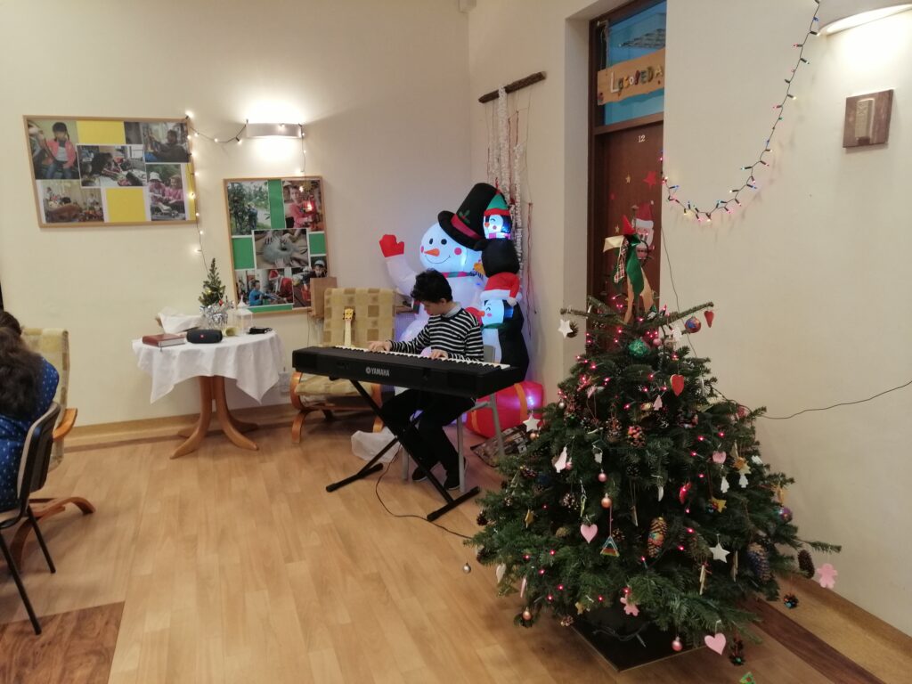 Adam gra kolędy na organach. Obok stoi choinka.