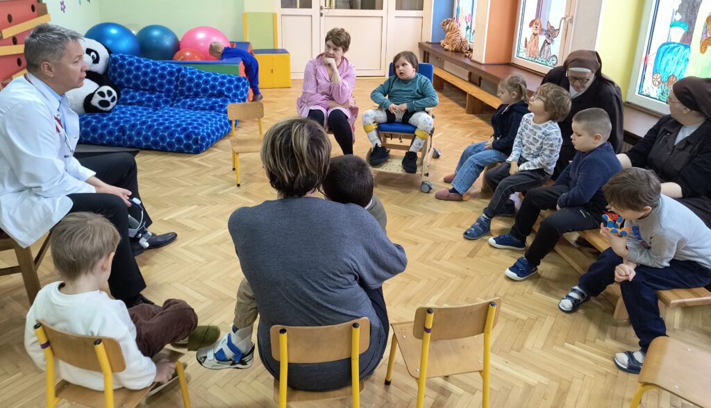 Dzieci siedzą w kole z lekarzem w białym fartuchu.