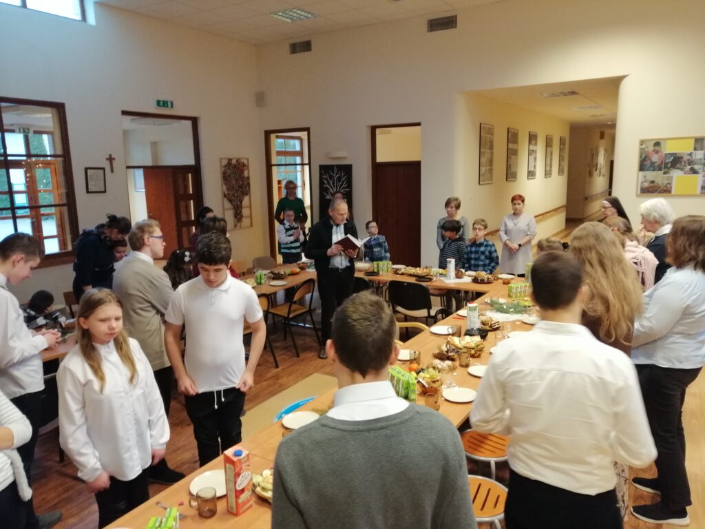 Pan Andrzej czyta fragment Ewangelii wg św. Łukasza o narodzeniu Jezusa. Wszyscy stoją i uważnie słuchają.