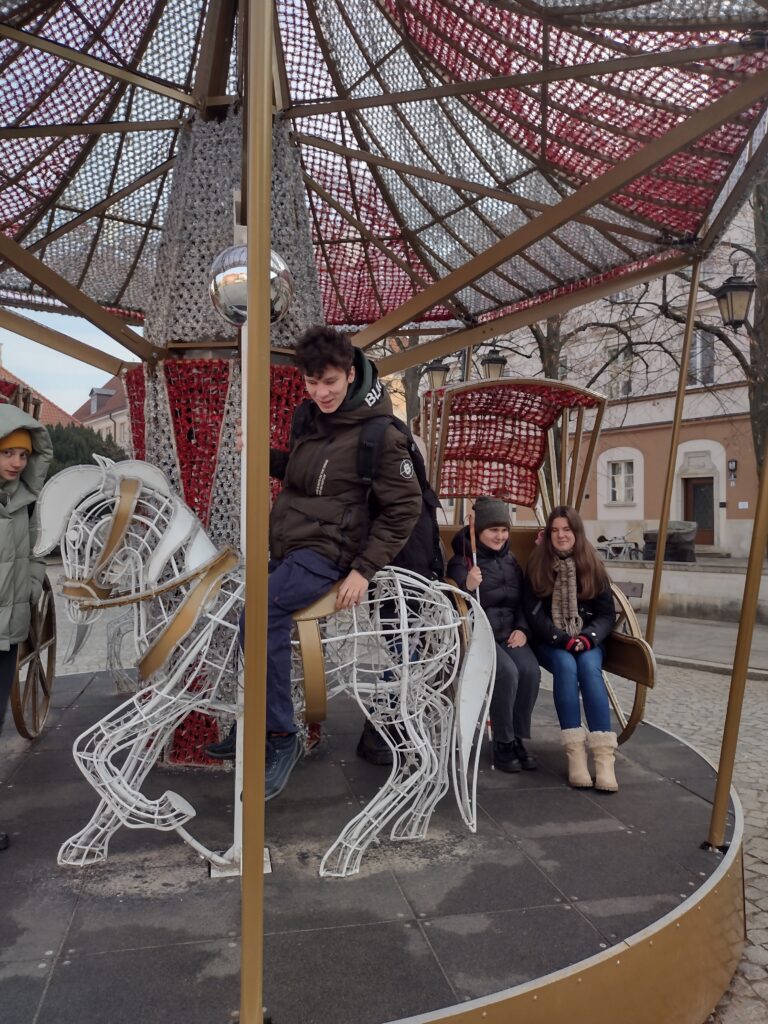 Karuzela świąteczna na starówce. Uczeń siedzi na koniu. Uczennice siedzą w karecie.