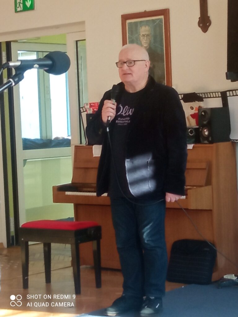 Pan Marek stoi przy pianinie z mikrofonem w ręku