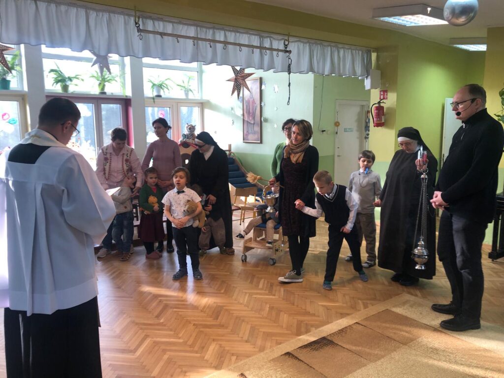 Dzieci i pracownicy przedszkola wraz z księdzem modlą się na bawialni