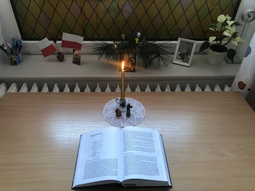 Leżące na stole Pismo Święte, a za nim zapalona świeca stojąca na ozdobnej serwetce