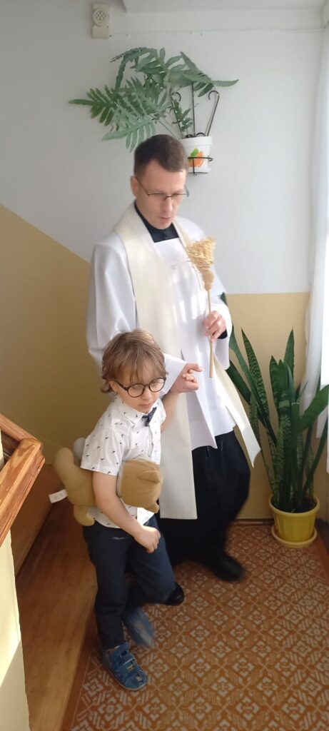 Ksiądz trzymający kropidło schodzi z chłopcem ze schodów 