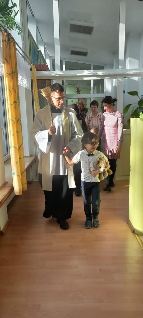 Ksiądz prowadzony przez chłopca święci pomieszczenia, za nimi wszyscy uczestnicy kolędy
