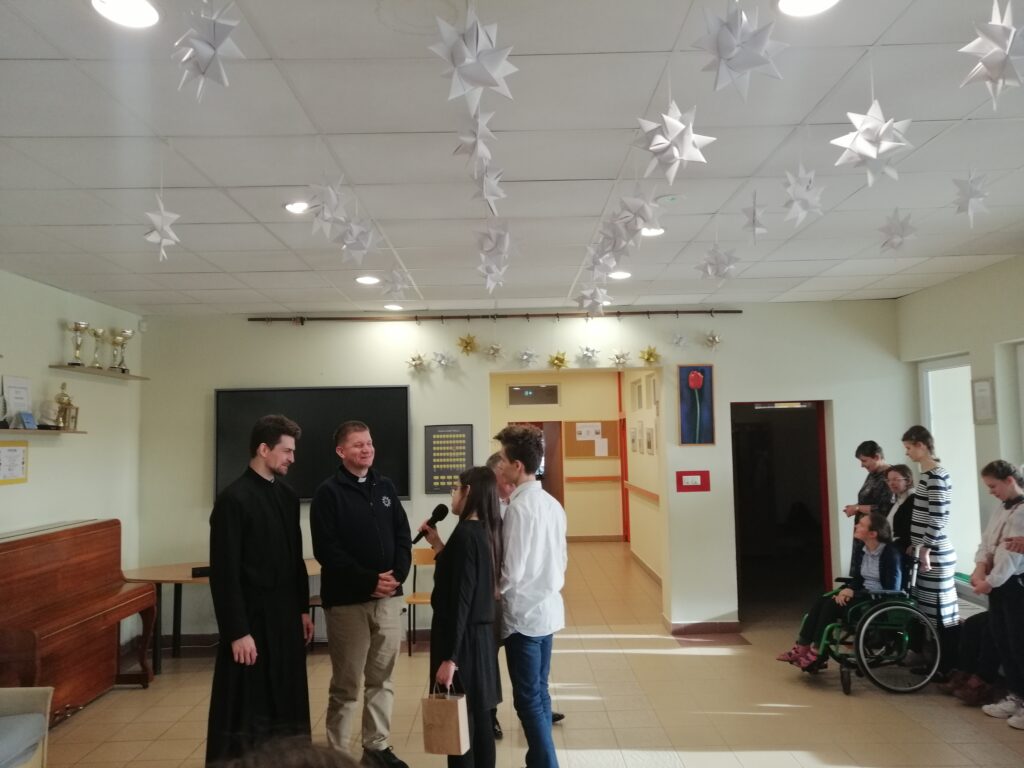 Dwoje uczniów w towarzystwie dyrektora dziękują braciom za świadectwo wręczając upominki.