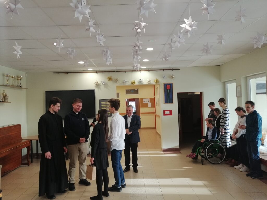 Dwoje uczniów w towarzystwie dyrektora dziękują braciom za świadectwo wręczając upominki. Na twarzach widać rado sc i poruszenie.