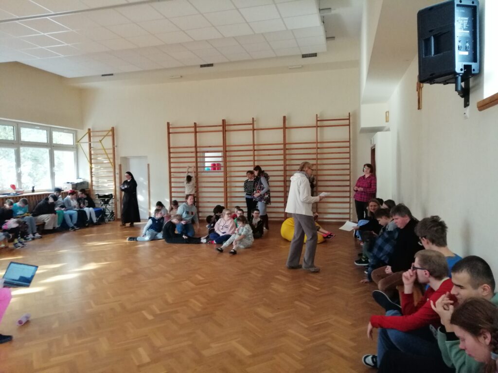 Na sali gimnastycznej uczniowie piątych klas słuchają pytania związanego z odtworzonym utworem.