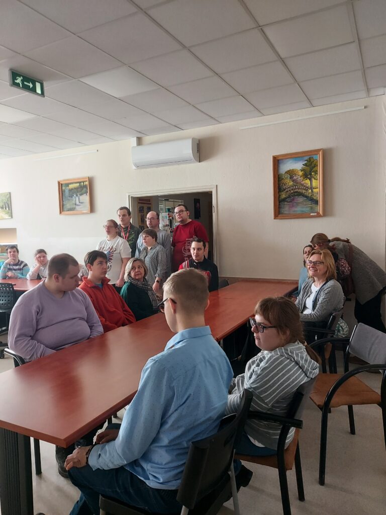 Uczniowie siedzą przy stole i słuchają piosenki w wykonaniu uczestników warsztatów