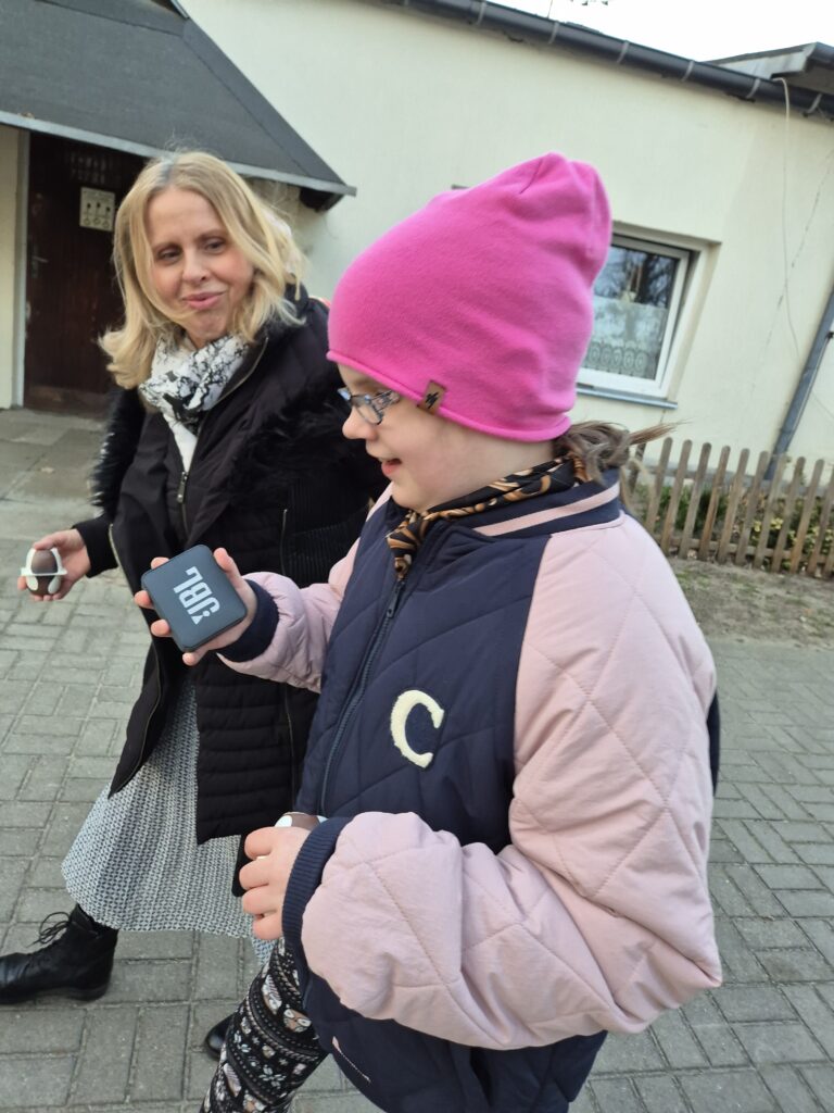 Ania trzyma w ręku głośnik bluetooth JBL w trakcie spaceru w towarzystwie pani Małgosi