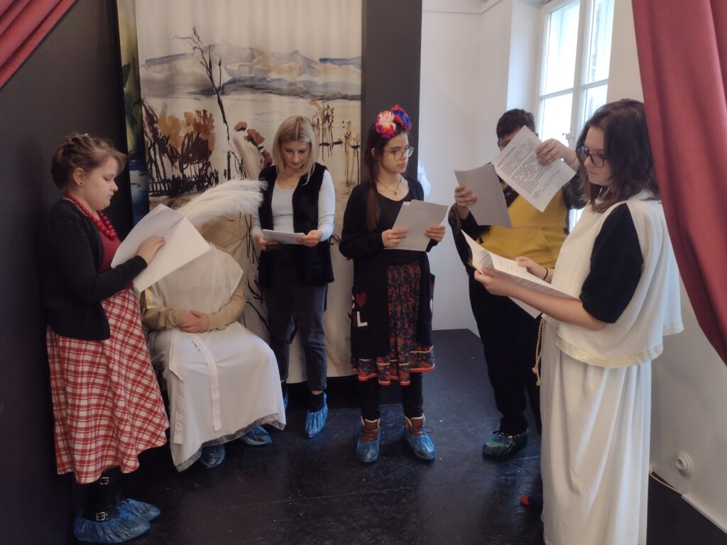 Uczniowie przebrani w stroje do miniatury dramatycznej. Stoją obok siebie i przygotowują się do przedstawienia.