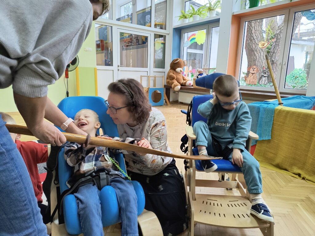 Uśmiechnięty chłopiec ogląda wiosło. Obok chłopiec na krzesełku.