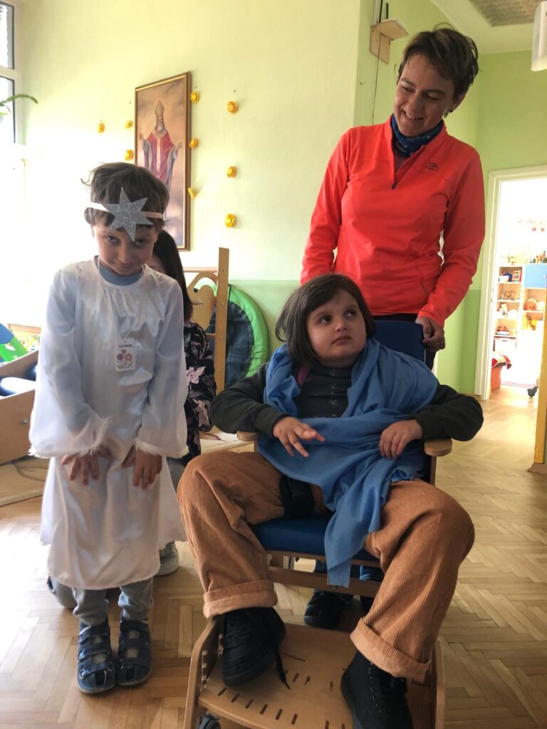 Dziewczynka okryta niebieską
chustą obok chłopiec w białym ubraniu z gwiazdą na czole z tyłu nauczycielka