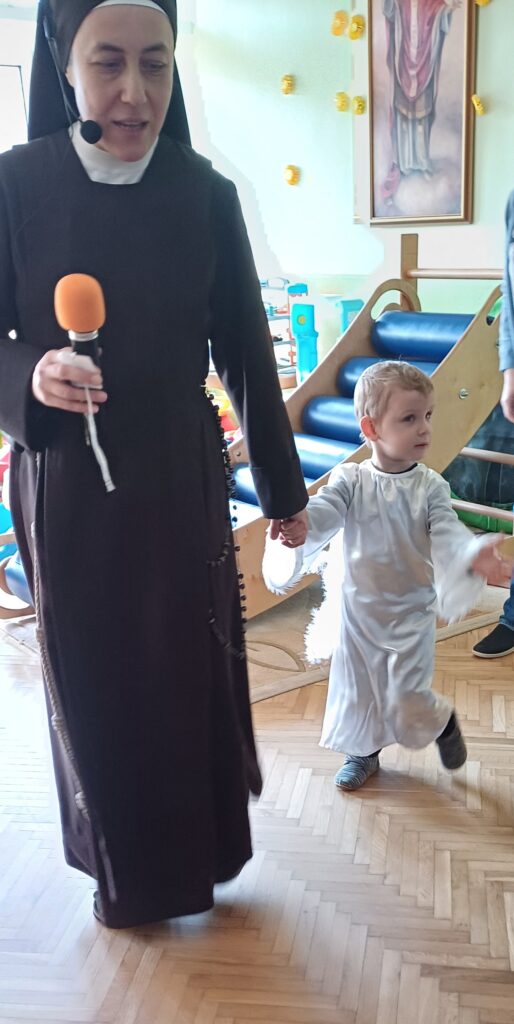 Siostra prowadzi za rękę chłopca w stroju anioła.