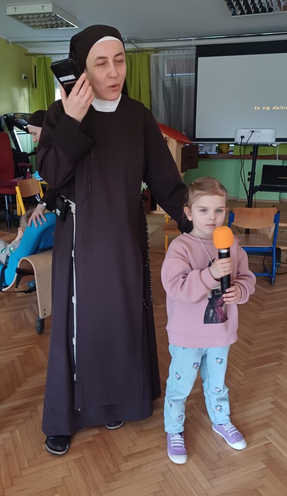 Siostra z głośnikiem przy uchu obok dziewczynka z mikrofonem,